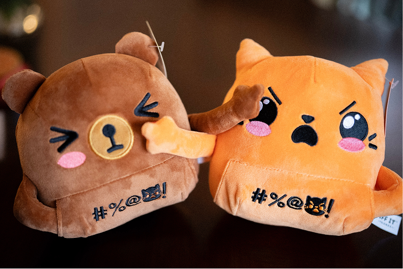 Bernard the brown bear and Jackie the orange cat plush side by side, Bernard's paw on Jackie's cheek