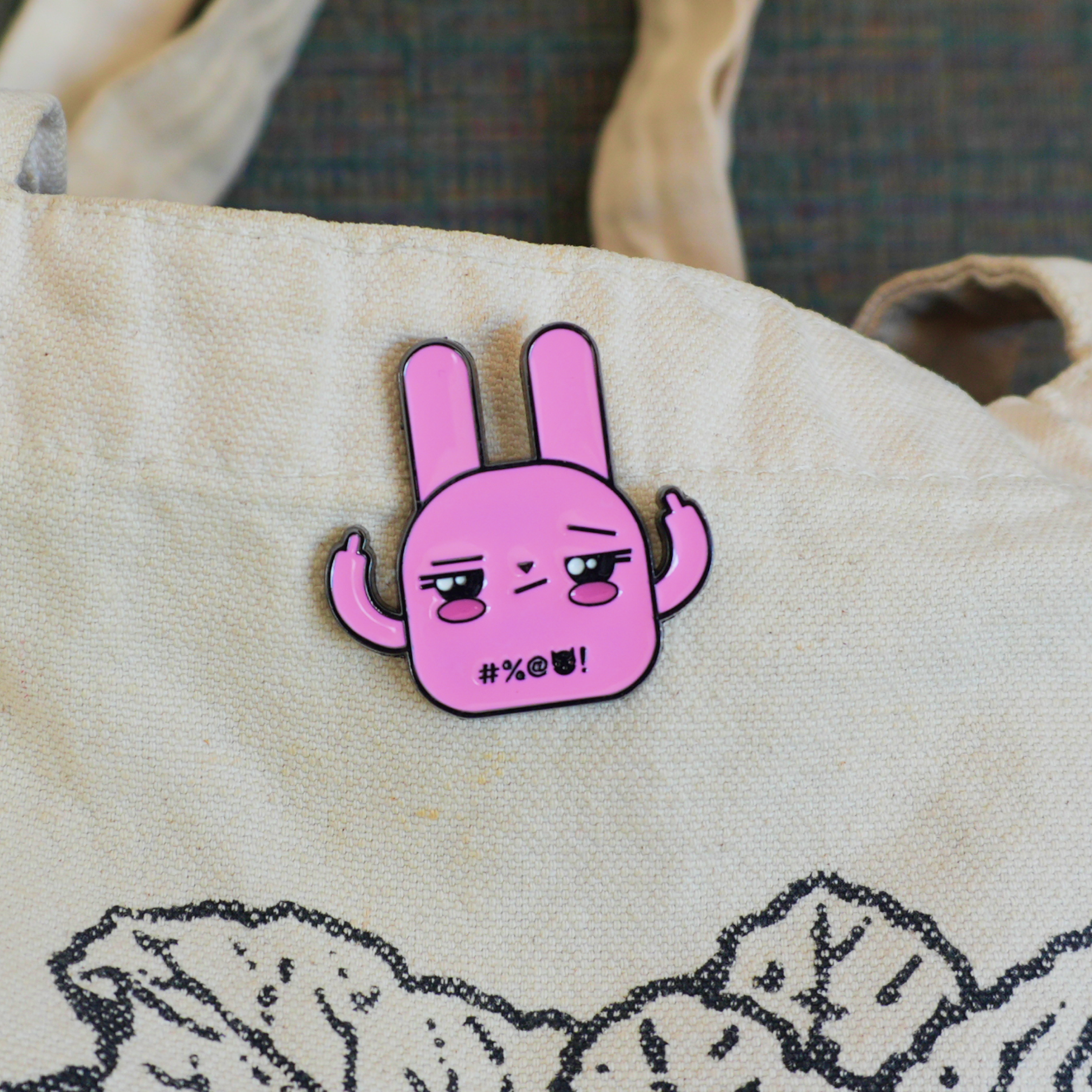 Pink bunny enamel pin with middle fingers up on beige tote bag