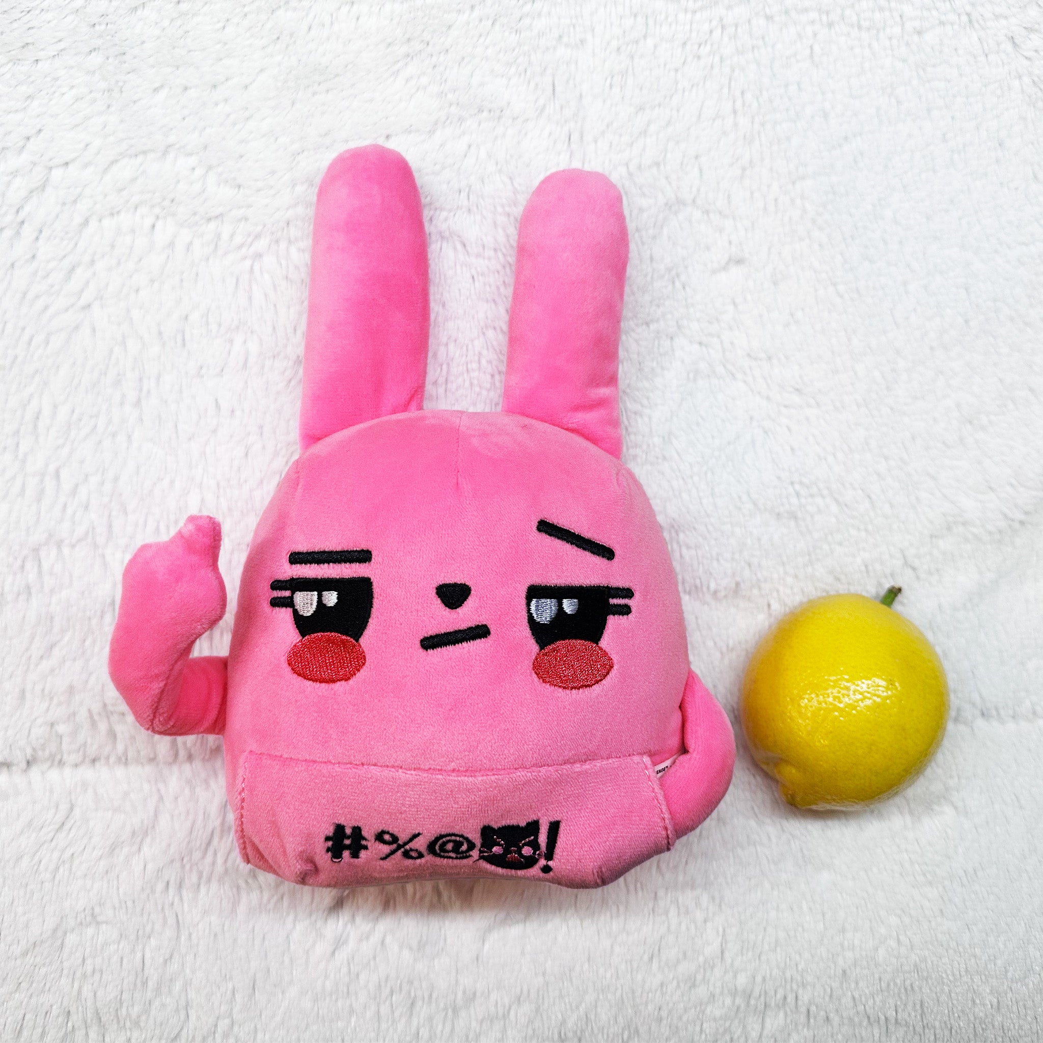 Pink bunny plush, one middle finger raised, lying face up next to a lemon.