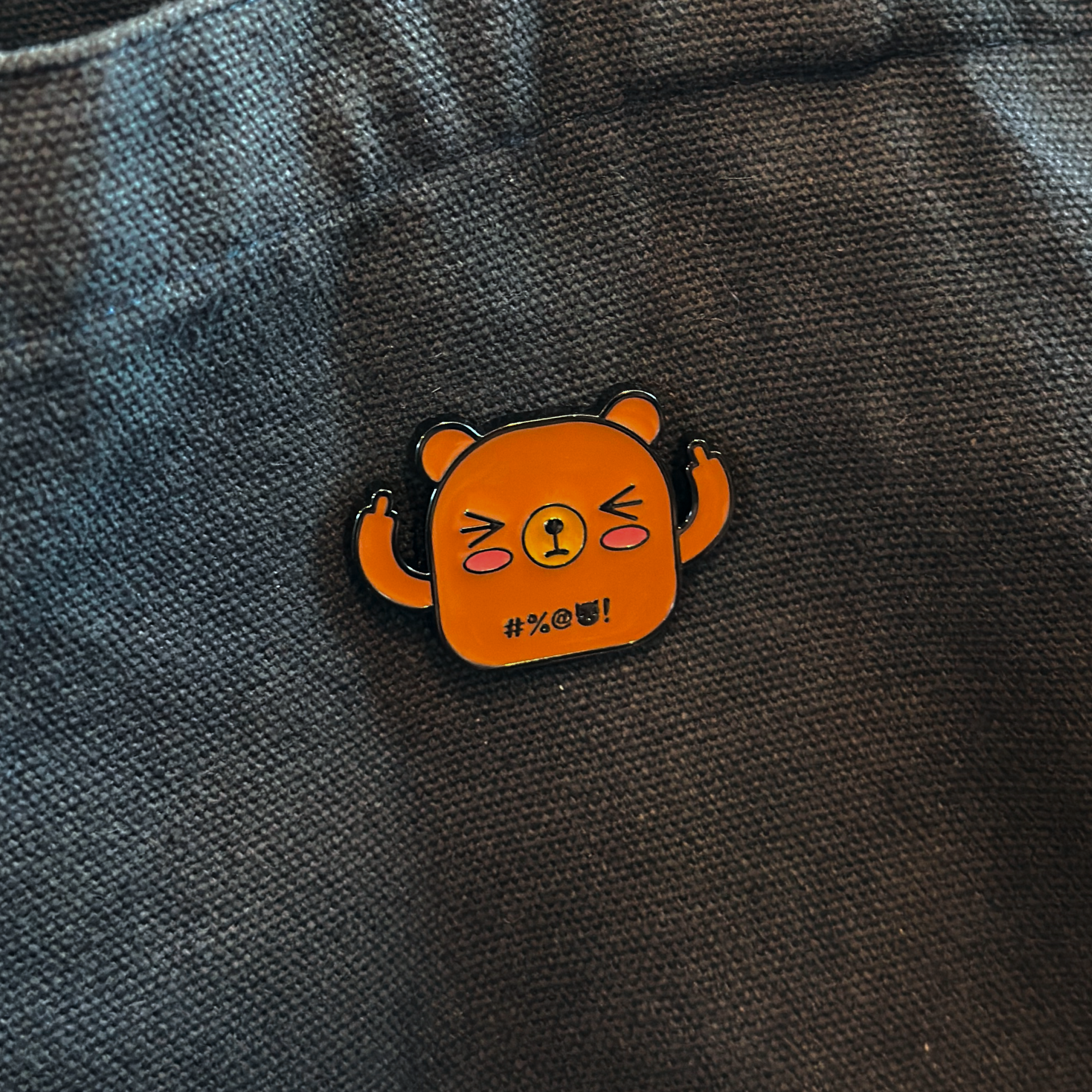 Brown bear enamel pin, middle fingers up, on dark tote bag