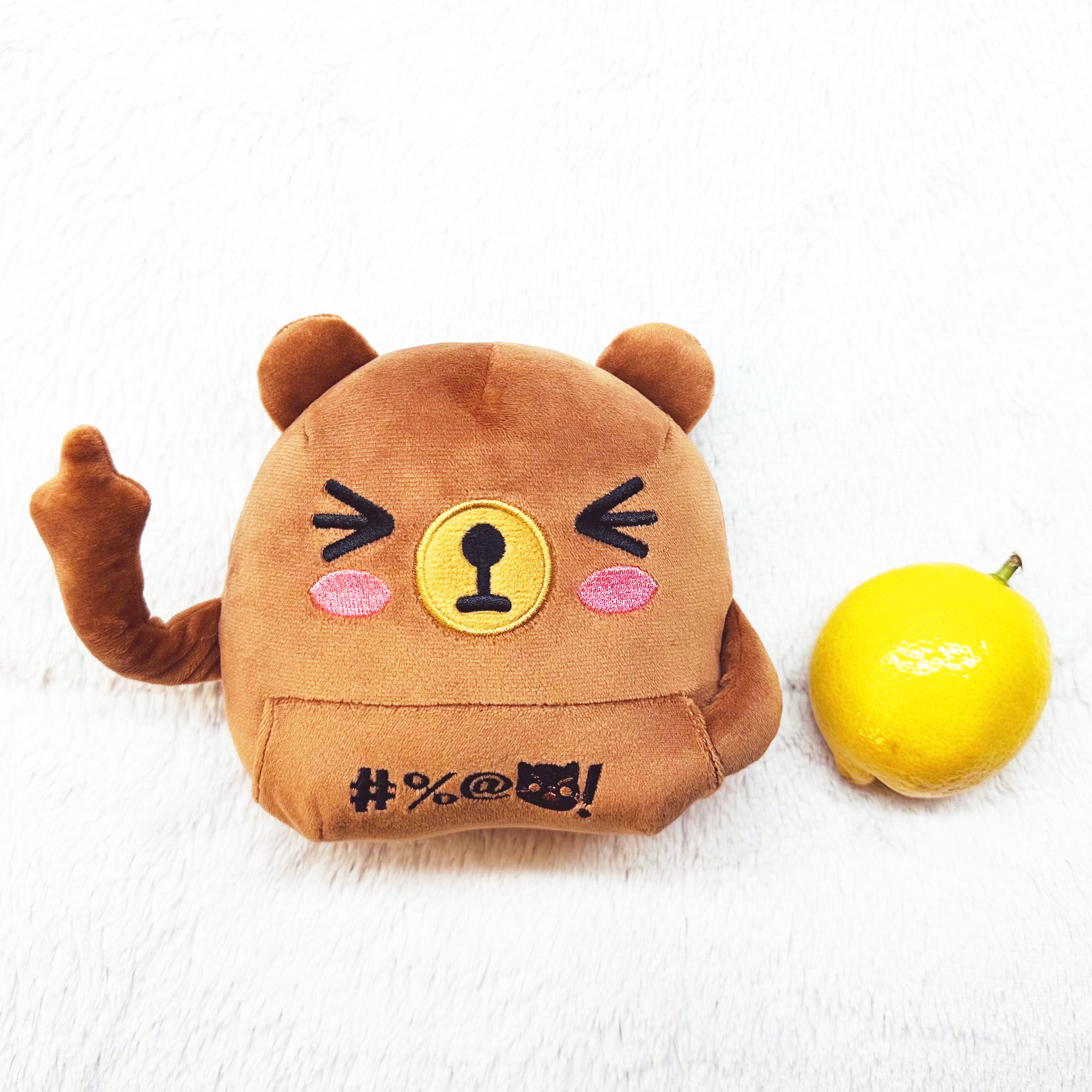 Brown bear plush, one middle finger raised, lying face up next to a lemon.