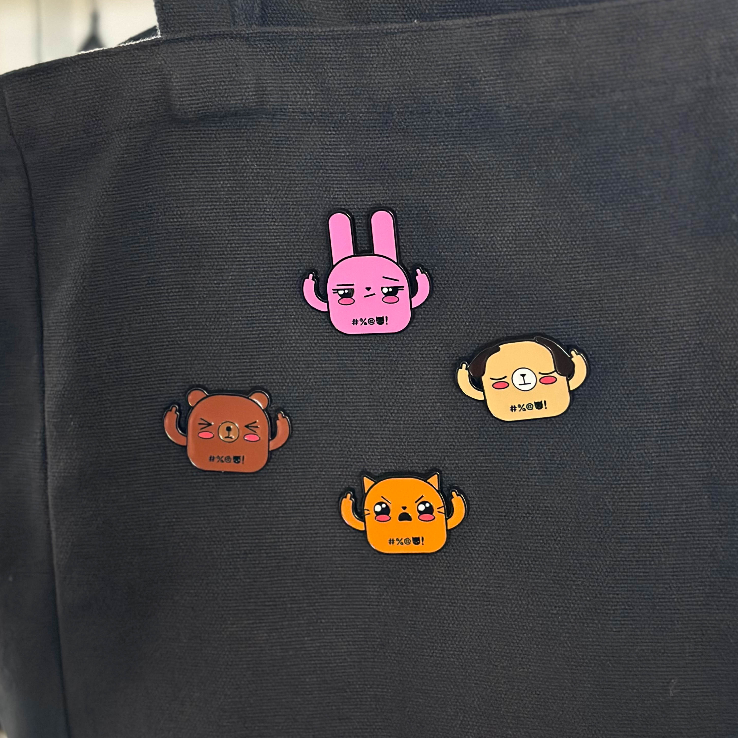 Pink bunny enamel pin, brown bear enamel pin, beige dog enamel pin, and orange cat enamel pin, front view on black tote bag