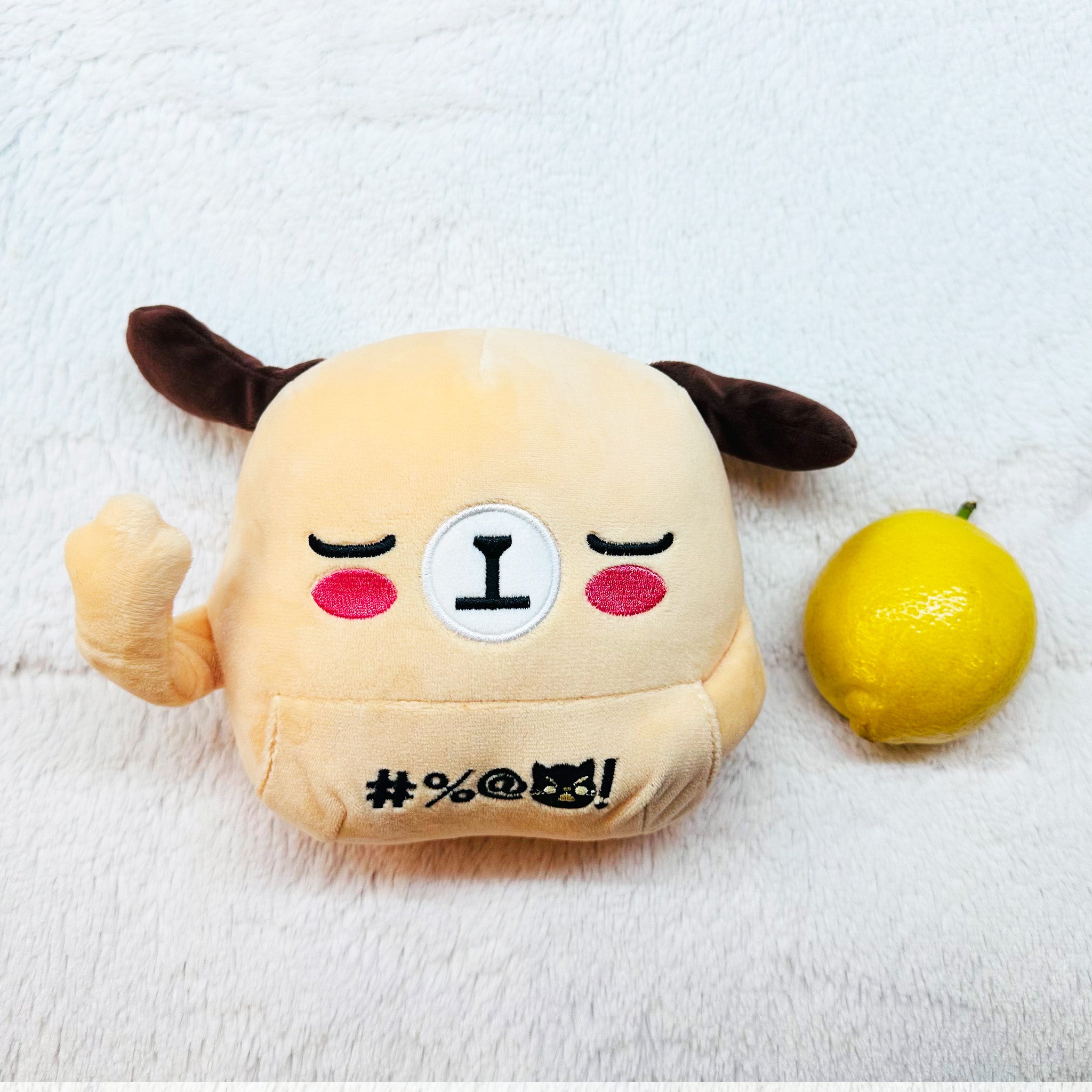 Beige dog plush, one middle finger raised, lying face up next to a lemon.