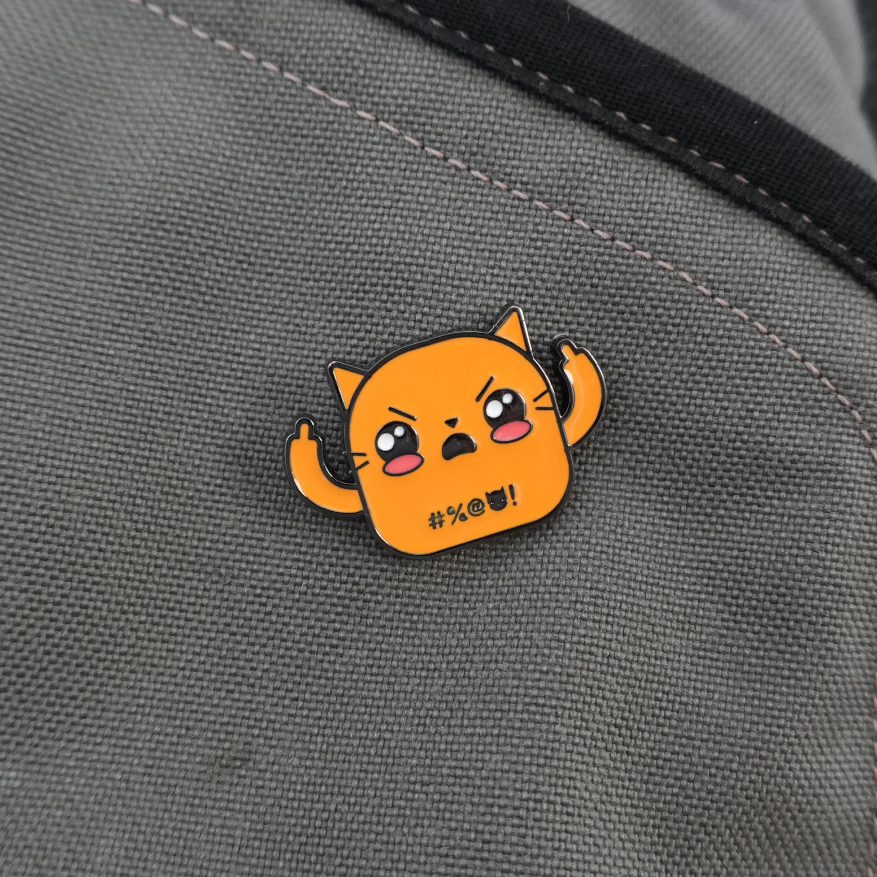 Orange cat enamel pin with middle fingers up on grey backpack
